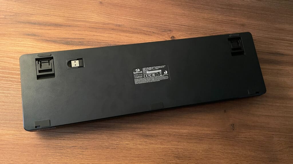 Bottom view of the Redragon Wyvern K761 Pro mechanical keyboard showing the adjustable feet and built-in storage compartment for the wireless dongle.