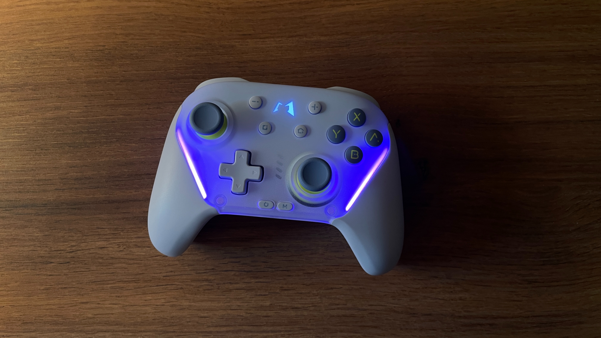Photo of the Mobapad Chitu 2 HD Silent Edition controller taken in a well-lit environment, showing its RGB backlighting effects on the buttons and stick areas, with the illumination clearly visible despite ambient light.