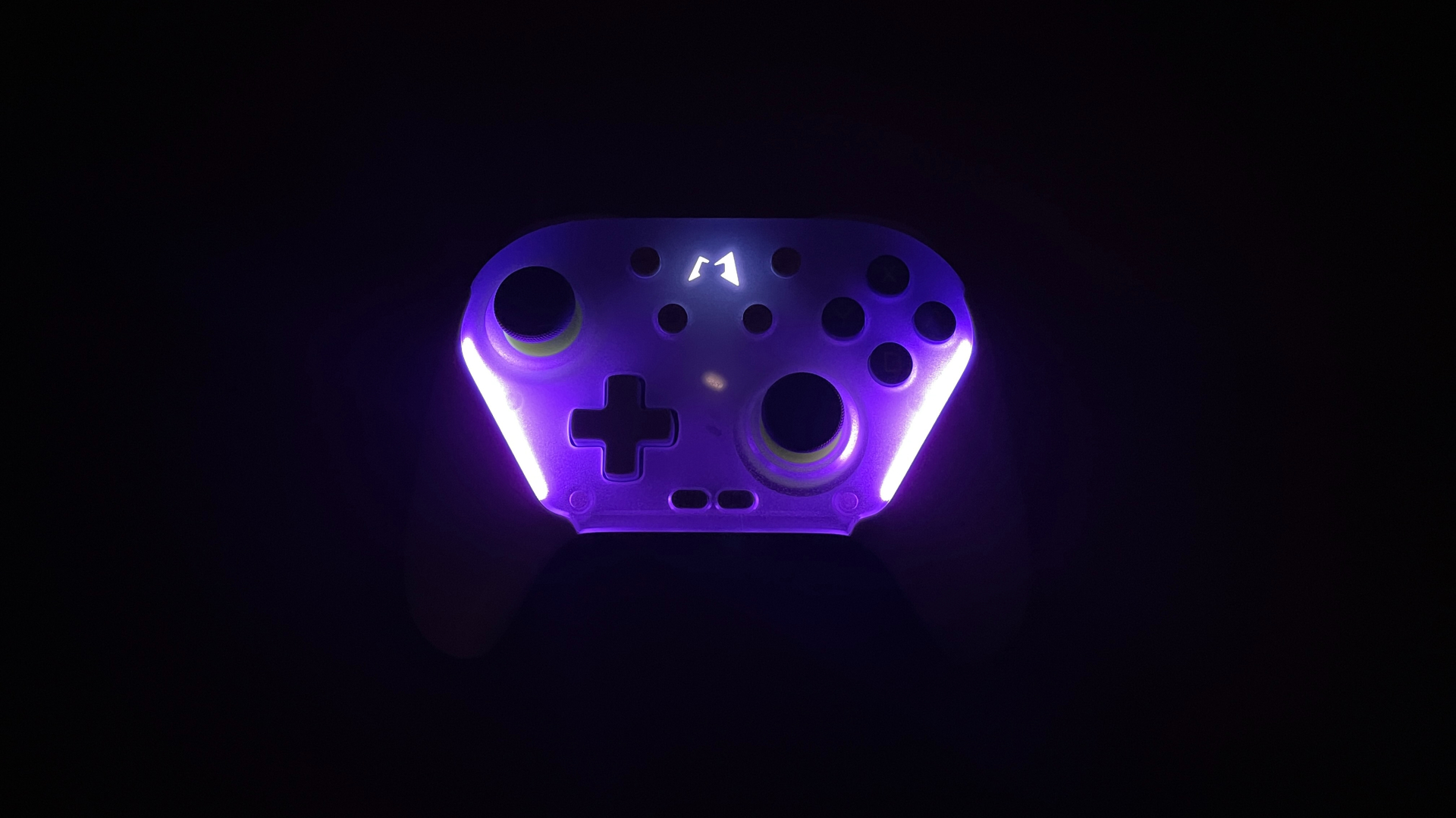 Close-up photo of the Mobapad Chitu 2 HD Silent Edition controller showing its RGB backlighting in a dark environment, highlighting the illuminated buttons and subtle glow around the sticks and body edges.