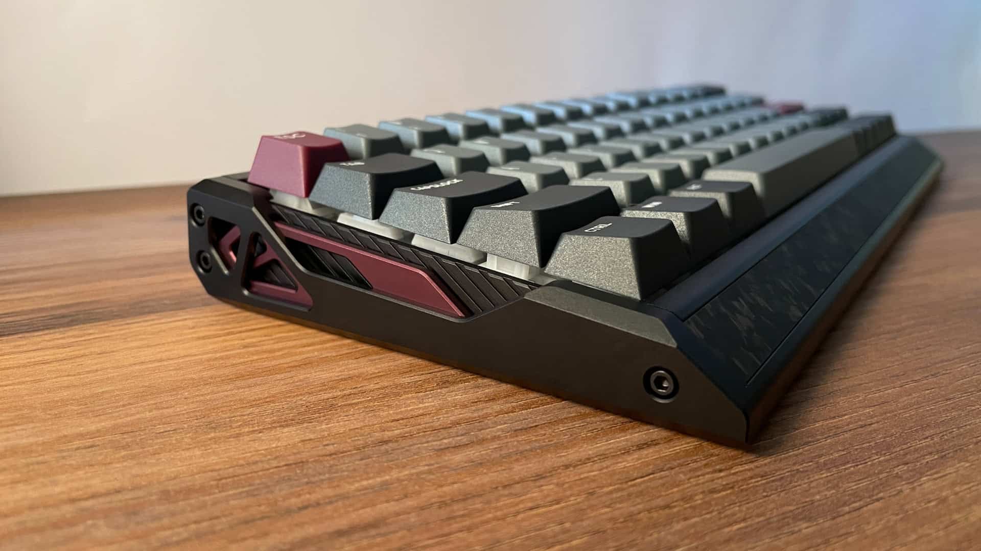 Side view of the IQUNIX EV63 mechanical keyboard highlighting its layered aluminum case design with visible structural divisions, exposed inner lines, and a deep burgundy middle section paired with matching accent keycaps.