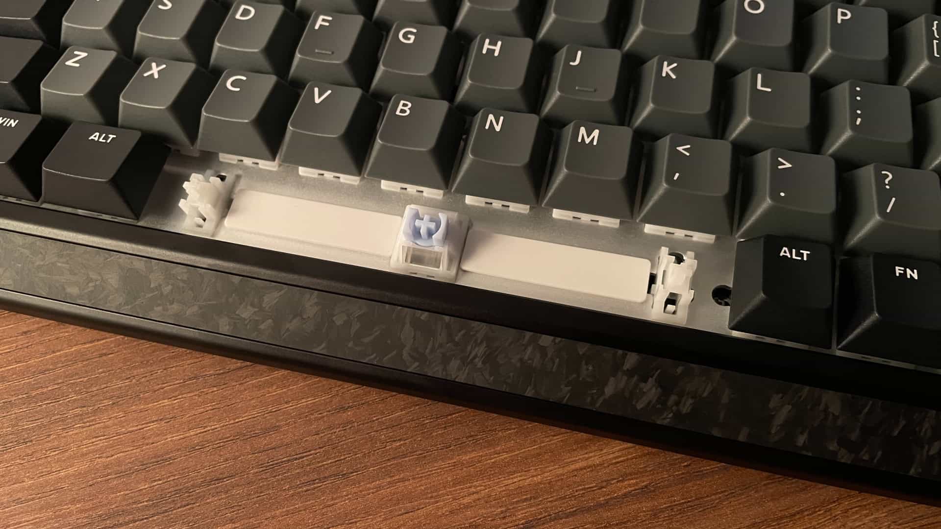 Close-up of the IQUNIX EV63 mechanical keyboard with the spacebar keycap removed, revealing extra damping pads underneath for improved sound.