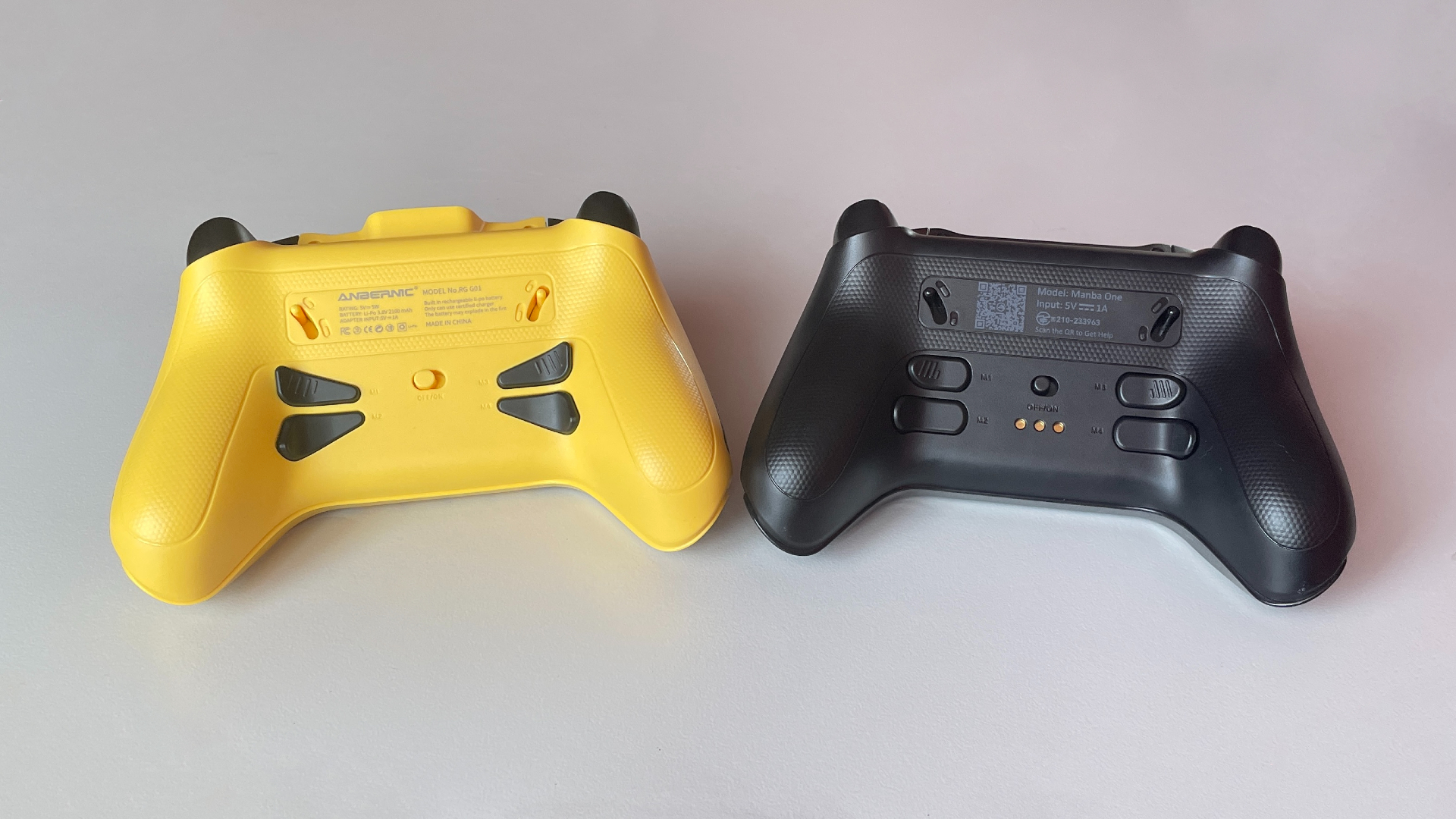 Rear view of the Manba One V2 and Anbernic RG G01 controllers shown side by side, highlighting the back design, triggers, and rear buttons.