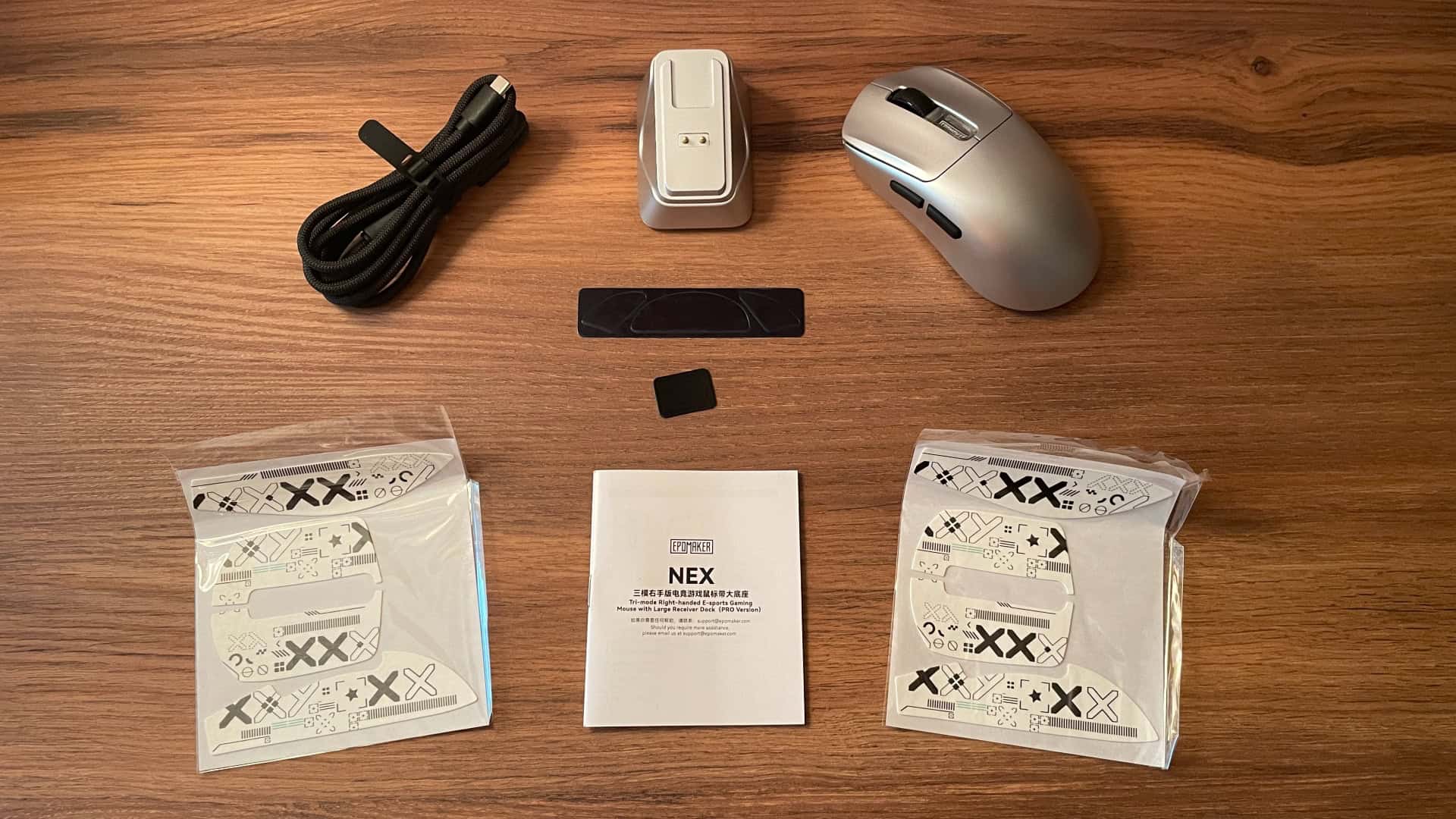 Everything included with the Epomaker Nex Pro: the mouse, magnetic charging dock with built-in 2.4 GHz receiver, braided USB-C cable, spare PTFE skates, two sets of grip tapes, and the user manual.