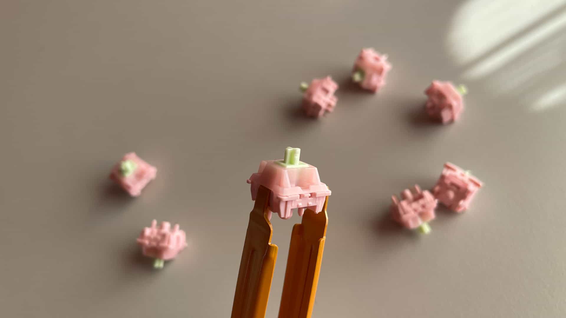 Close-up view of a KiiBoom x Strawberryjam1986 Strawberry Jello linear switch, showing its pink housing, green stem, and MX-style design.