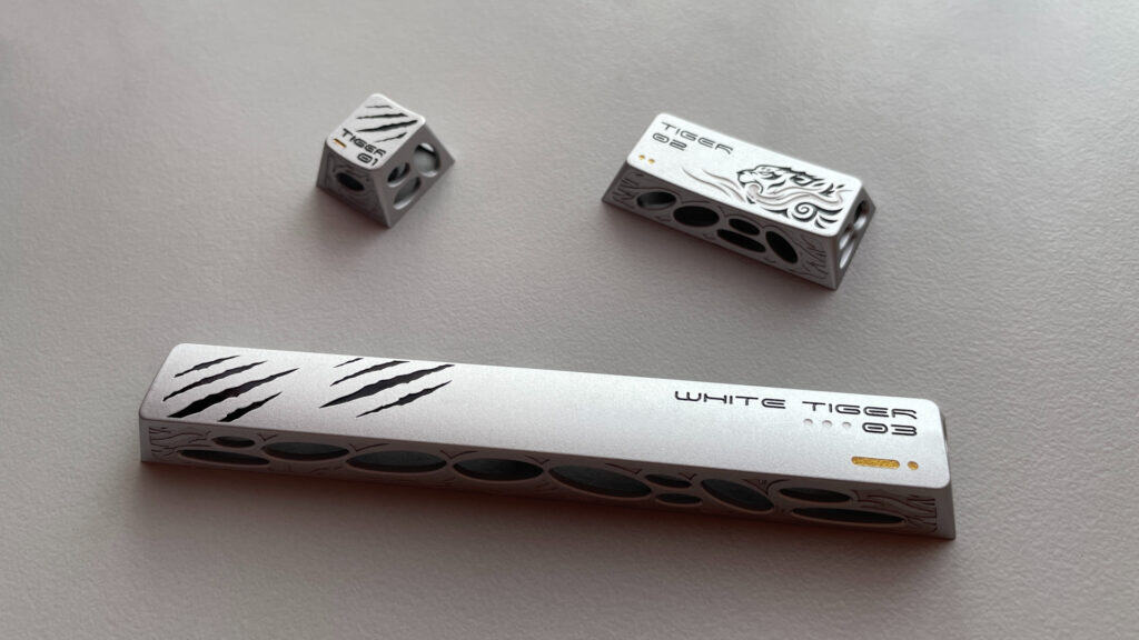 The aluminum artisan keycaps from the XVX White Tiger set displayed together, showcasing their engraved designs and painted details.
