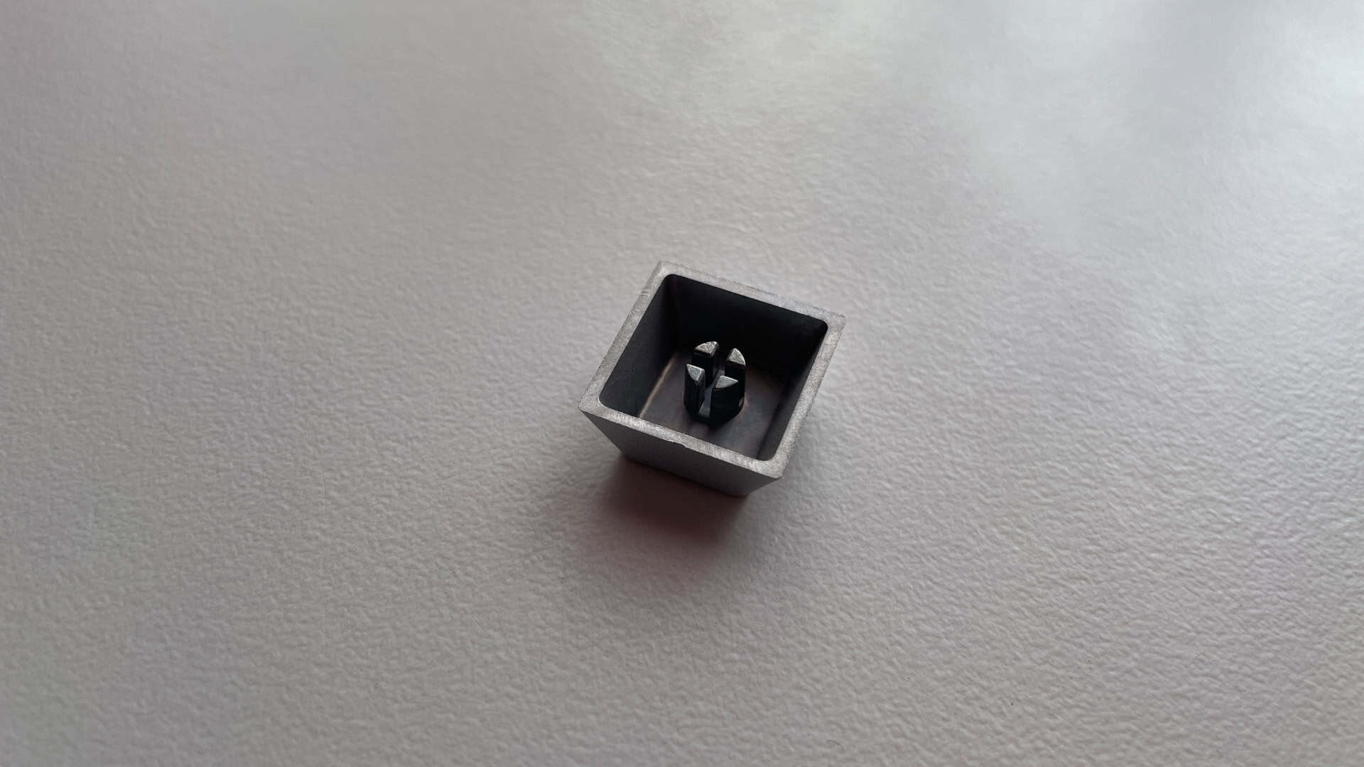 An aluminum keycap shown upside down to reveal its stem and internal construction.